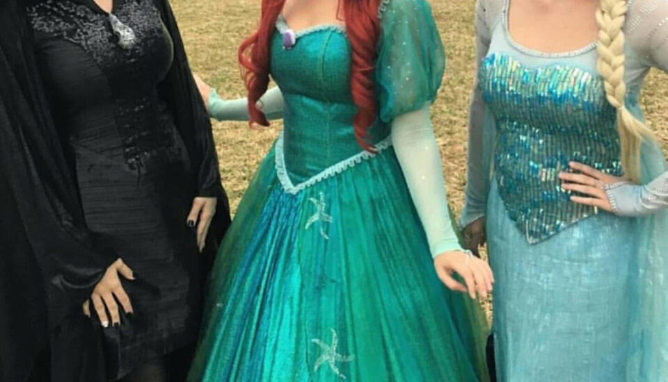 Three women dressed as popular Disney princesses posing outdoors.