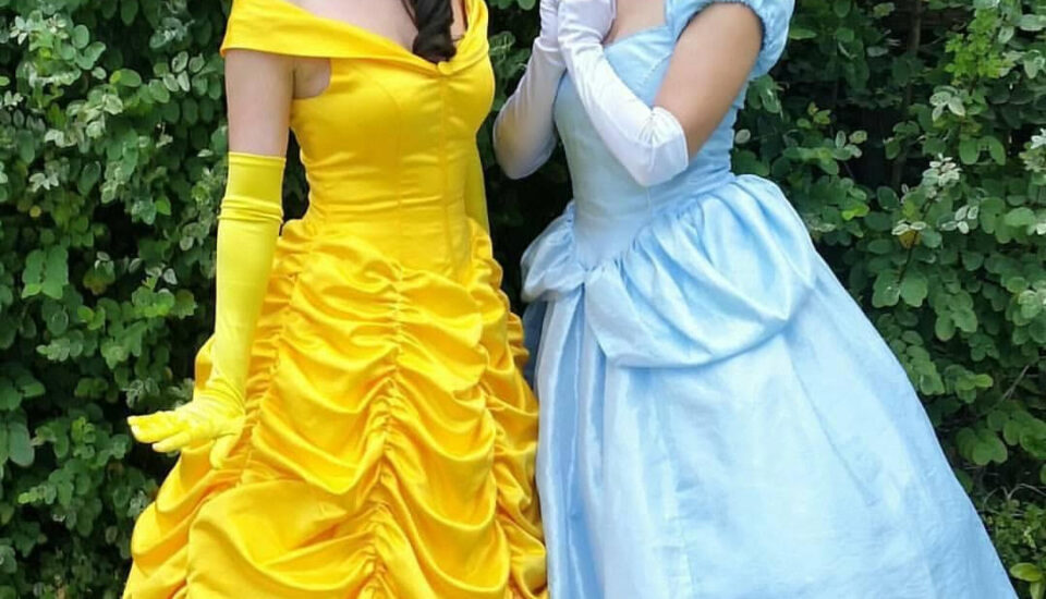 Two women dressed as Disney princesses in bright yellow and blue gowns.